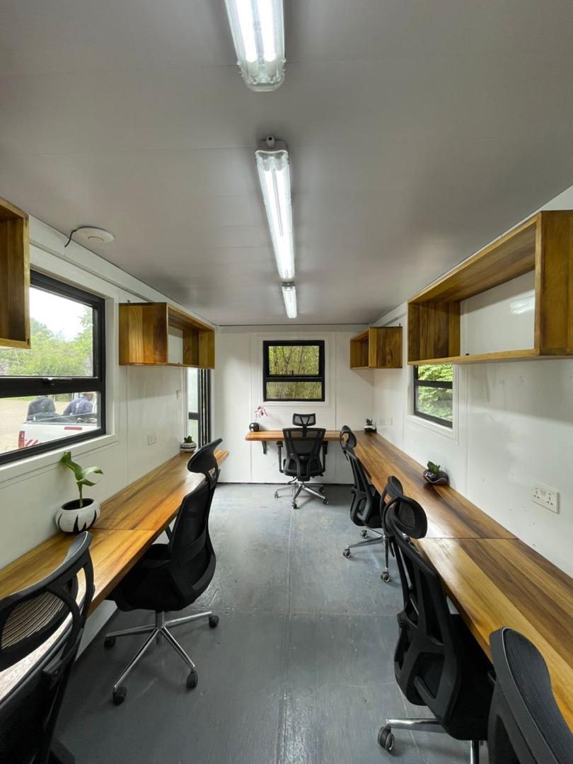 Converted shipping container office with timber-effect worktops, cupboards, windows and office seating